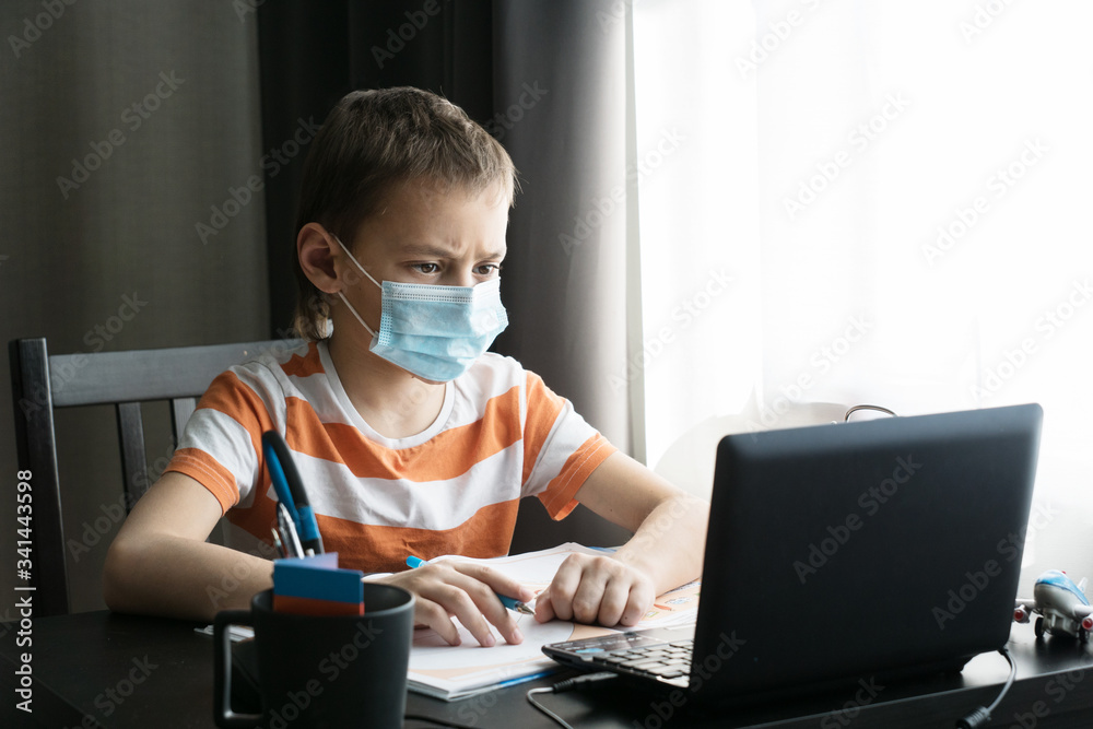 schoolboy in medical mask sits at his desk by computer,does his homework, remote education concept, stay home during coronavirus pandemic schoolboy in medical mask sits at his desk by computer,does his homework, remote education concept, stay home during coronavirus pandemic