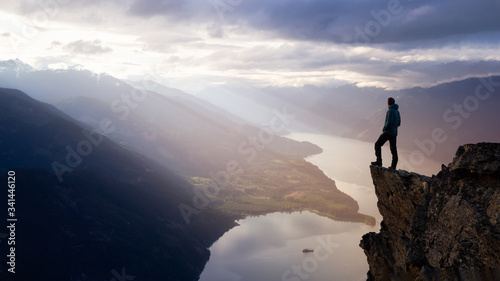 Fantasy Adventure Composite with a Man on top of a Mountain Cliff with Dramatic Landscape in Background during Sunset or Sunrise. Landscape from British Columbia, Canada. photo