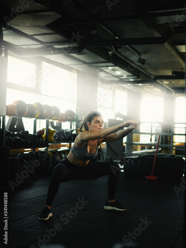 Three quarter angle full length shot of determined and fit young woman doing squats during cross training workout in gym