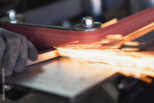 Industrial tool worker grinds a square steel pipe on a rotating belt sander
