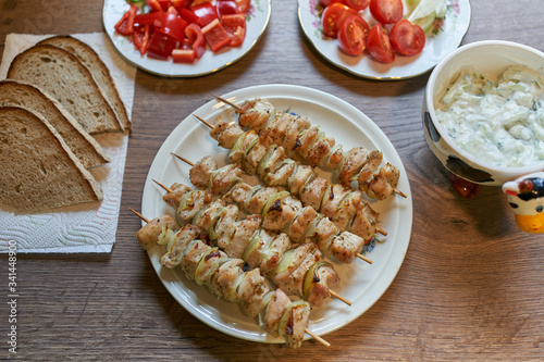 Grilled skewers consist from chicken breast meat served with chopped fresh vegetables like tomatoes, onion, sweet red pepper and cucumber, slices of rustic bread and yogurt dip. Light and healthy dish