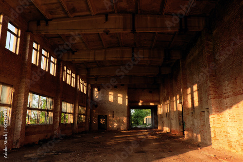 A large abandoned industrial building is lit by light from the windows. Large red brick building.