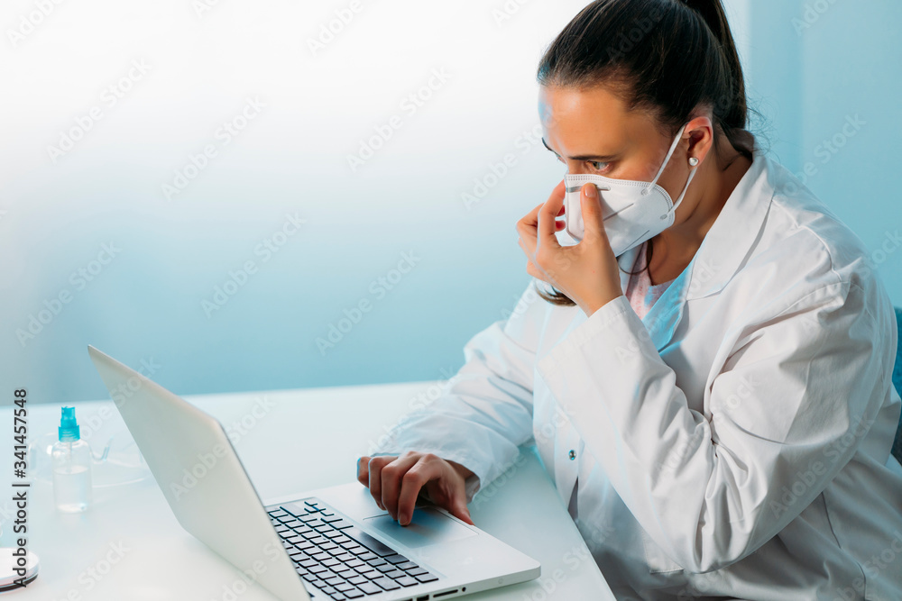 Portrait of young female doctor in white coat at workplace with mask to protect against coronavirus