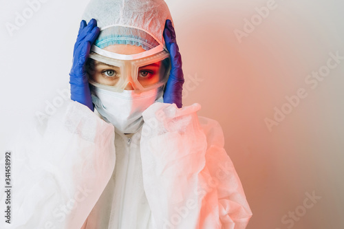 Doctor in protective uniform, reperitor, glasses, gloves on a blue background in neon light. A close-up portrait of a doctor in red neon. A tired man is battling a coronavirus. COVID 19 photo