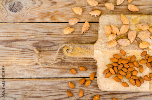 Peeled and unpeeled almonds on wooden background.