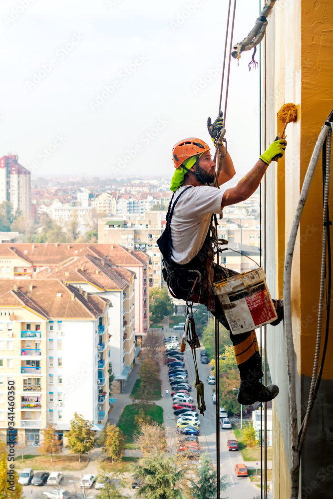 Φωτογραφία Industrial climber hanging on the rope while painting the exterior facade wall of the tall apartment building