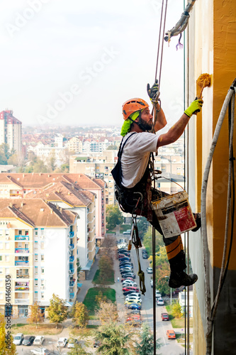Industrial climber hanging on the rope while painting the exterior facade wall of the tall apartment building. Industrial alpinism and high risk work scene concept image