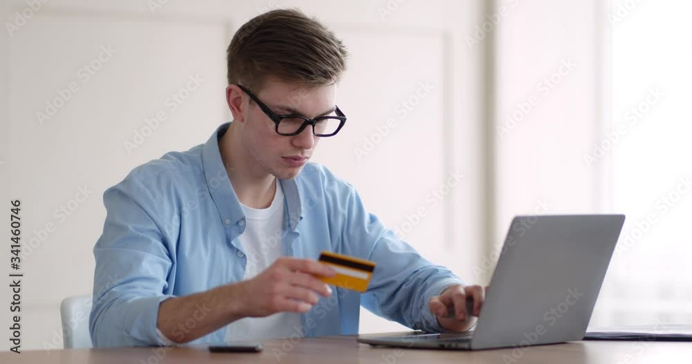 Young man typing number of credit card on laptop