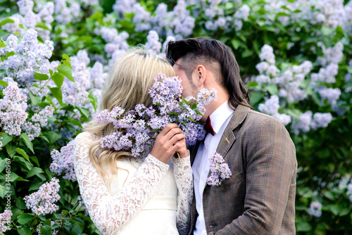A loving couple kisses amid a blooming lilac