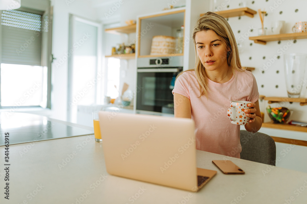 Portrait of young blonde woman drinking coffee and using laptop early in the morning. Young woman is working from home, because she is in self quarantine. Portrait of young blonde woman drinking coffee and using laptop early in the morning. Young woman is working from home, because she is in self quarantine.