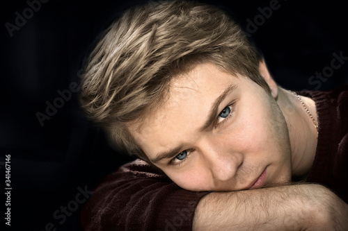 A young man with blond hair put his head on his hand and looks at you carefully
