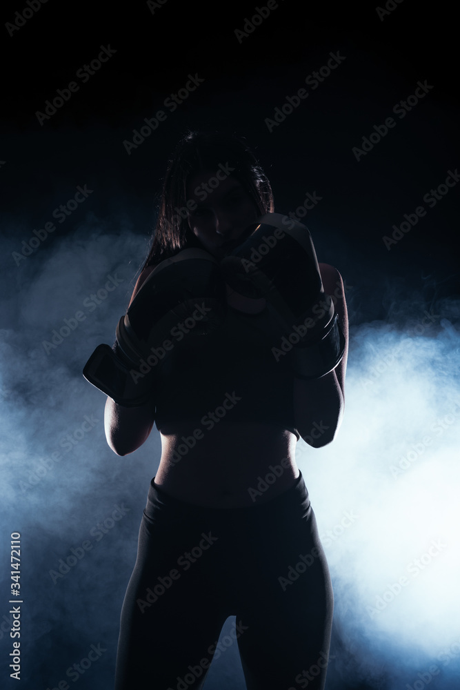 Silhouette portrait with white smoke in the background of a female model with boxing gloves