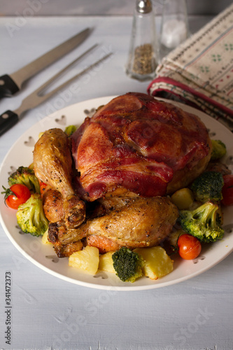 Whole roast chicken with breasts wrapped in bacon and vegetables: potatoes, broccoli and tomatoes. vertical image