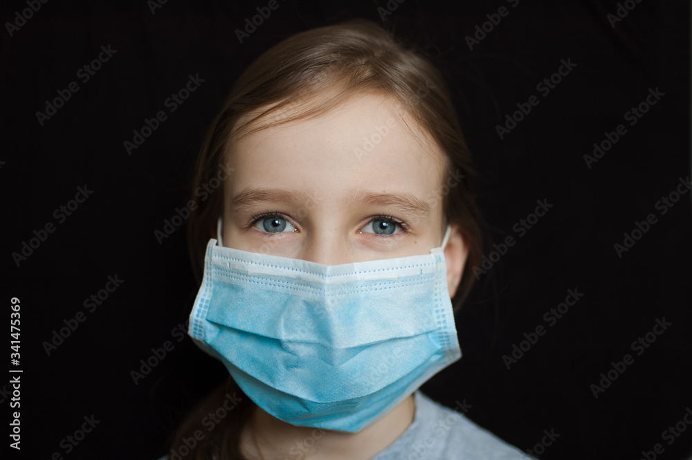 Coronavirus Covid-19 outbreak. Little blonde girl wearing light blue disposable mask for protection of virus on black background in studio. Quarantine concept Coronavirus Covid-19 outbreak. Little blonde girl wearing light blue disposable mask for protection of virus on black background in studio. Quarantine concept