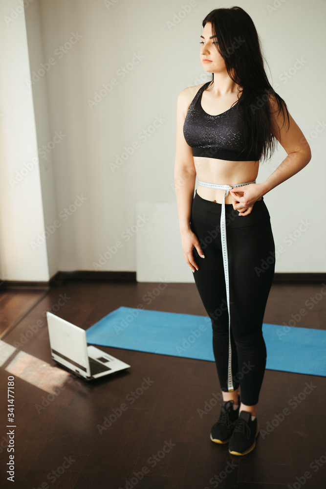 Obraz premium Successful weight loss, diet, home training, motivation and healthy lifestyle. Woman with perfect slim body measuring her waistline with tape