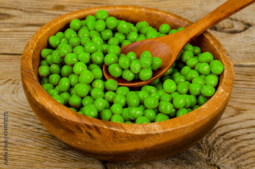 Wooden bowl with canned green peas on table.