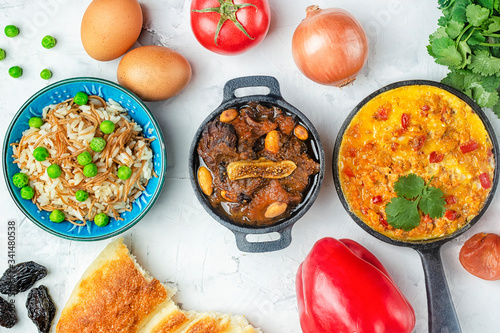 On a gray background, three dishes of national Turkish cuisine. Menemen, Kuzu mutancana and pilaf. The ingredients are laid out around. Photo with copy space. photo