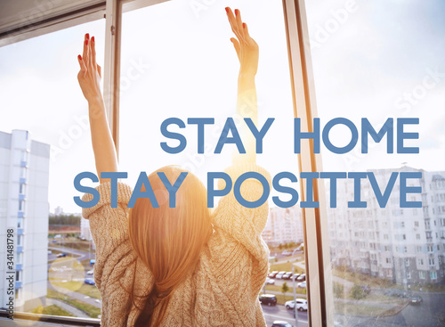 Woman near window raising hands facing the sunrise at morning photo