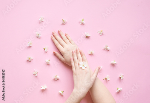 Hands of a woman with white flowers on a pink background. Natural cosmetics product and hand care  moisturizing and wrinkle reduction. Flat Lay and skincare concept.