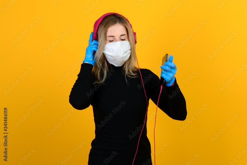Portrait of a girl in a medical mask, which puts on a rubber glove. Yellow and grey background. Copy space. Portrait of a girl in a medical mask, which puts on a rubber glove. Yellow and grey background. Copy space.