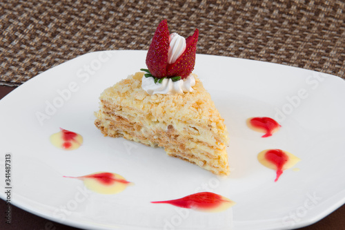 Slice of cottage cheese cake with butter cream decorated with Bizet and strawberries on a white large plate on a brown background