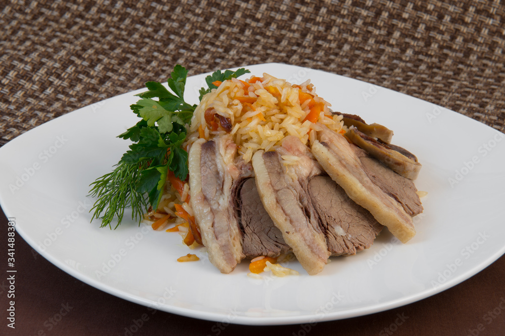 Long-grain rice pilaf with beautifully sliced fat veal garnished with dill and parsley on a white large plate on a brown background