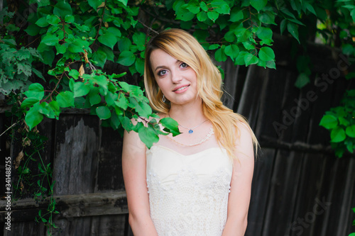 young, blonde girl, of Slavic origin, in a white dress of the bride against the background of summer green nature. A girl in a white dress among green trees in the forest