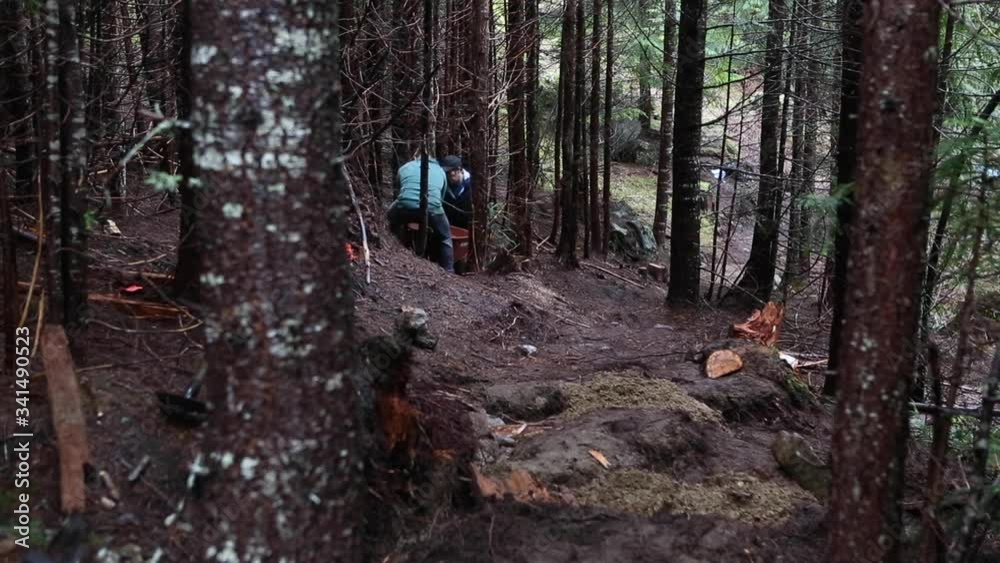 Two men pushing whellbarrow with dirt in forest, building a new trail.