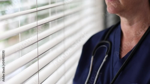 Stressed Doctor or Nurse On Break At Window Wearing Stethoscope and Scrubs. photo