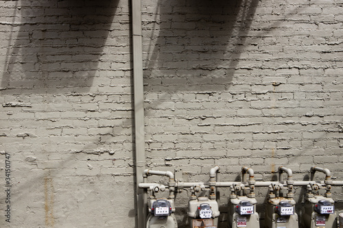 Grey painted brick wall including pipes and water meters with shadows from ac units above