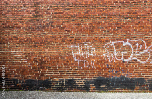 Light white Graffiti and black spray paint on an old yellow brown and red brick wall with grey asphalt road