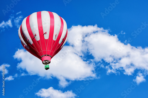 Red and white hot air balloon on the background of cloudy blue sky.