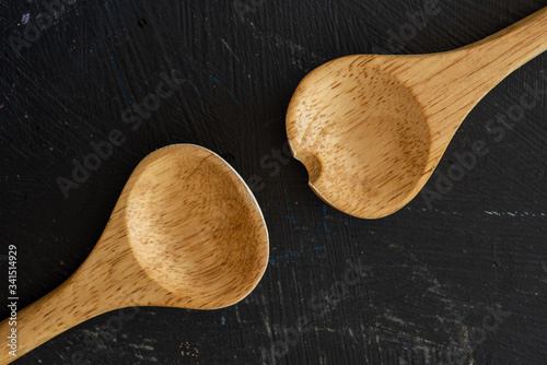 Top view of two wooden kitchen spoons in a black wooden cooking table