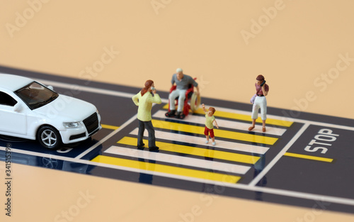 Miniature cars standing at a stop line and miniature people crossing crosswalks. 