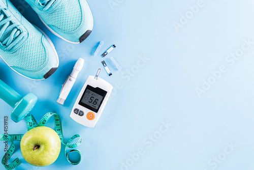 Healthy lifestyle, food and sport concept. Top view of diabetes tester set with athlete's equipment; measuring tape, green dumbbell and  fruit on bright blue pastel background.