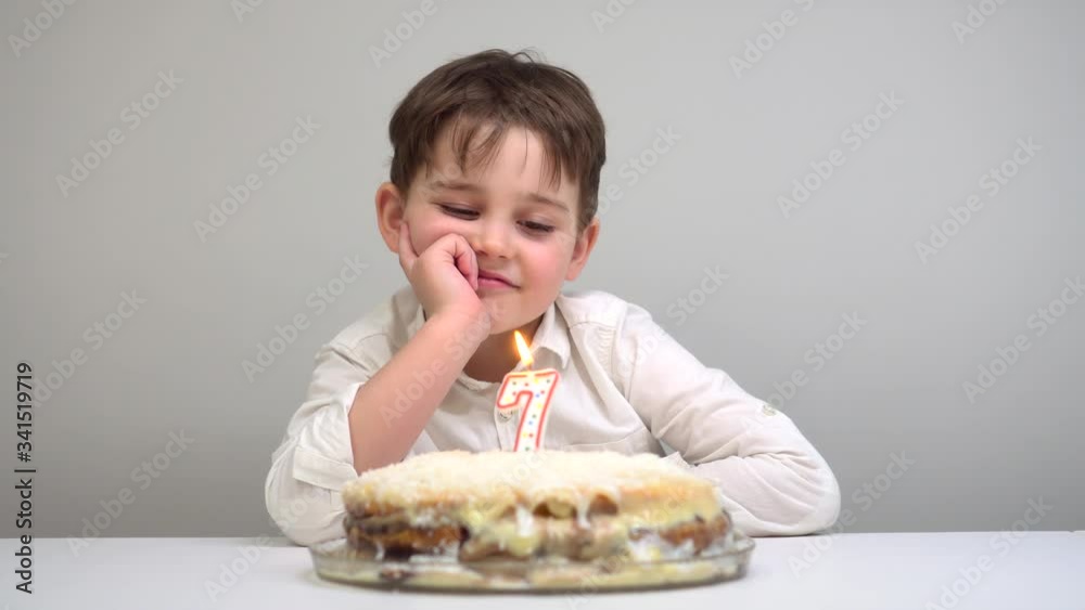 Sad boy looks to a cake with lighting candles on his birthday. Sad boy looks to a cake with lighting candles on his birthday.