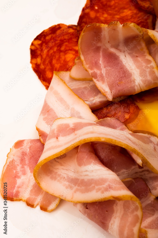 Slices of sausage and bacon on a white background. Close up. Slices of sausage and bacon on a white background. Close up.