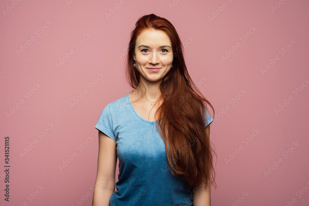 An attractive girl with red head is on the pink background. A girl is smiling on the background An attractive girl with red head is on the pink background. A girl is smiling on the background