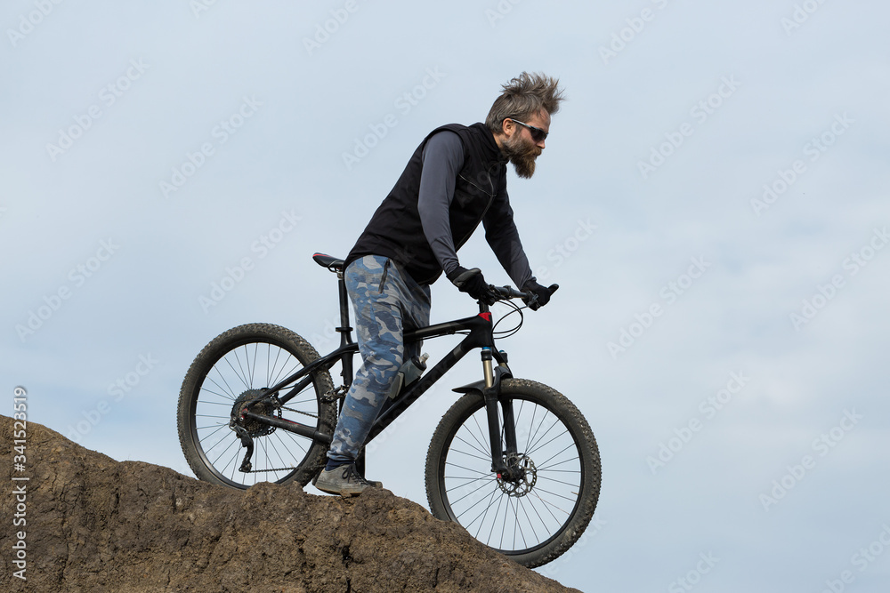 Sports brutal bearded guy on a modern mountain bike. Beautiful view from the mountain. Panoramic view for banner.