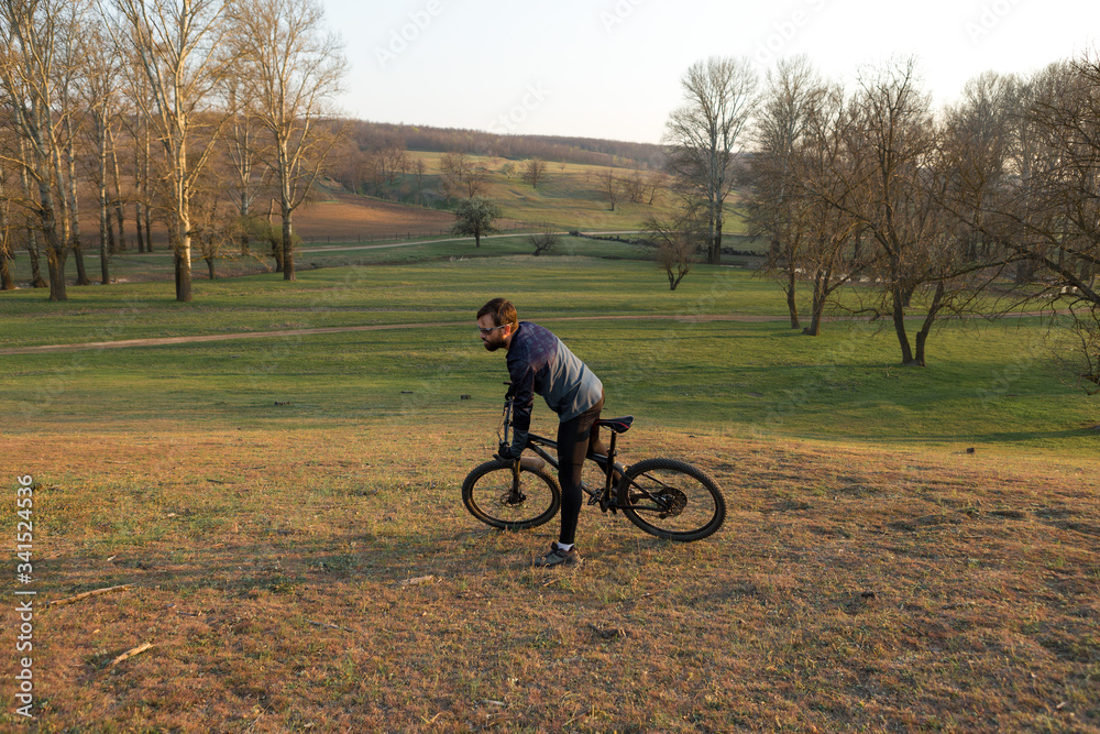 Fototapeta premium Cyclist in shorts and jersey on a modern carbon hardtail bike with an air suspension fork standing on a cliff against the background of fresh green spring forest