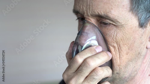 A man breathes oxygen using a mask. Close-up of an old man doing inhalation. photo