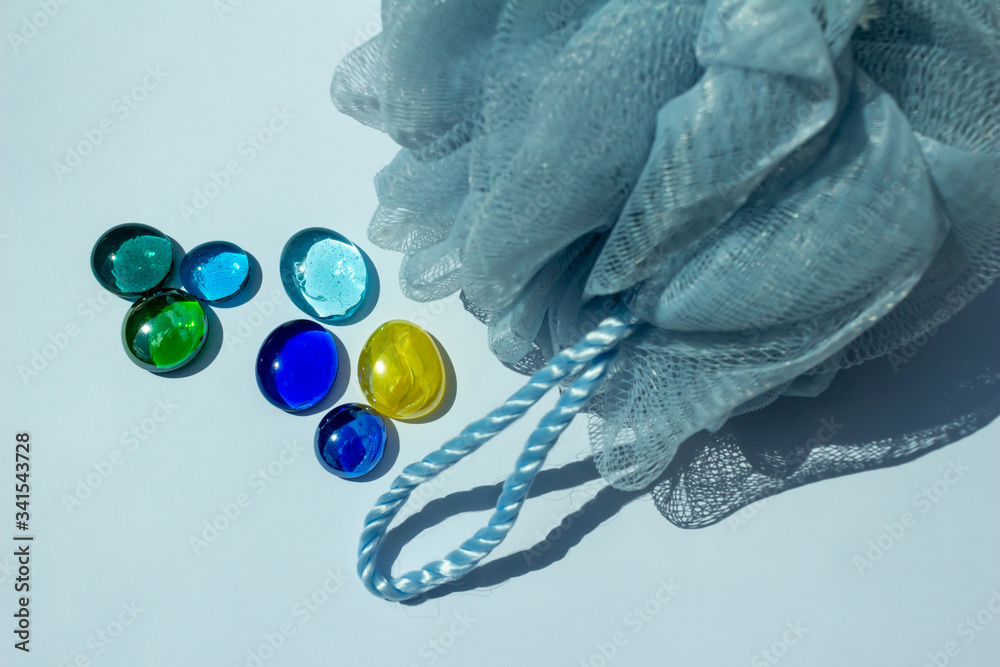 Fototapeta premium Blue mesh bath sponge abstract on white background with decorative blue and green glass beads, with copy space