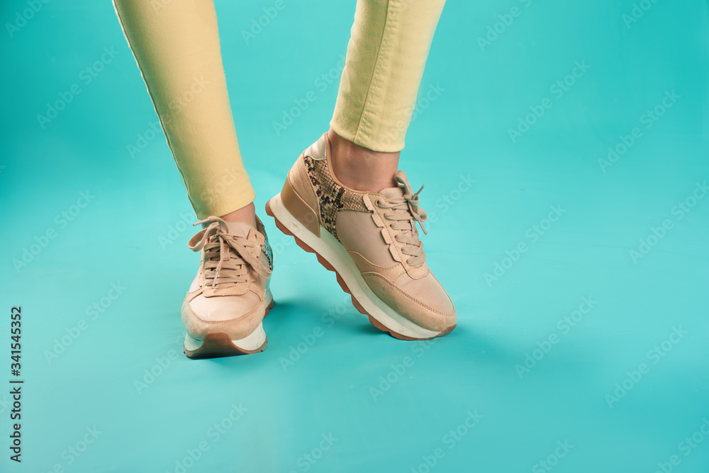 Close up photo of sneakers and yellow skinny jeans against an aqua background in a studio.