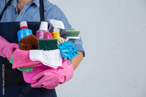 Young girl is holding cleaning product, gloves and rags in the basin on white background © artit