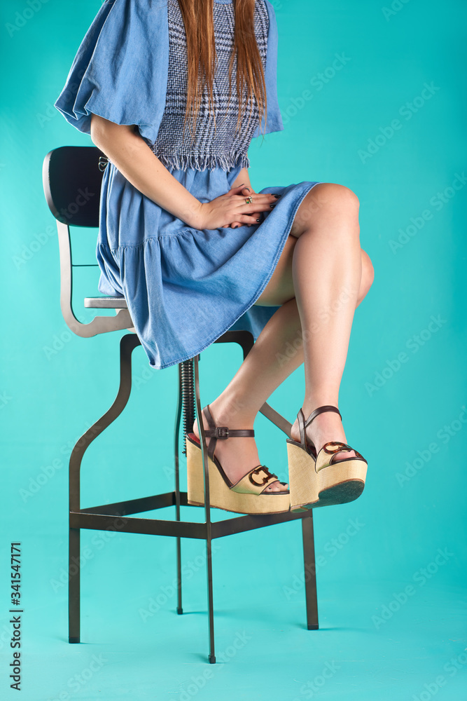 Cropped photo of a woman with a blue dress sitting on a high black ...