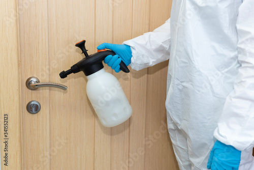 Woman or man in protective gloves and suit holds sanitizer and cleans metallic door knob. Office disinfection against new type of respiratory infection coronavirus covid-19