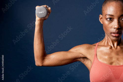 Active black woman lifting a dumbbell on blue background