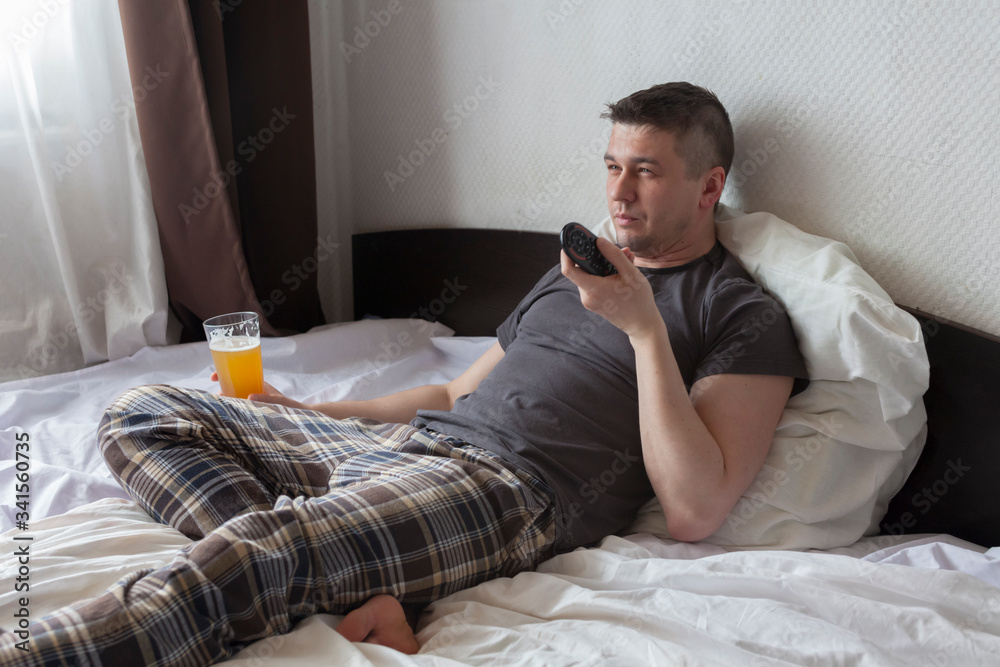 man in bed with beer watching TV. Alcoholism from boredom during Covid