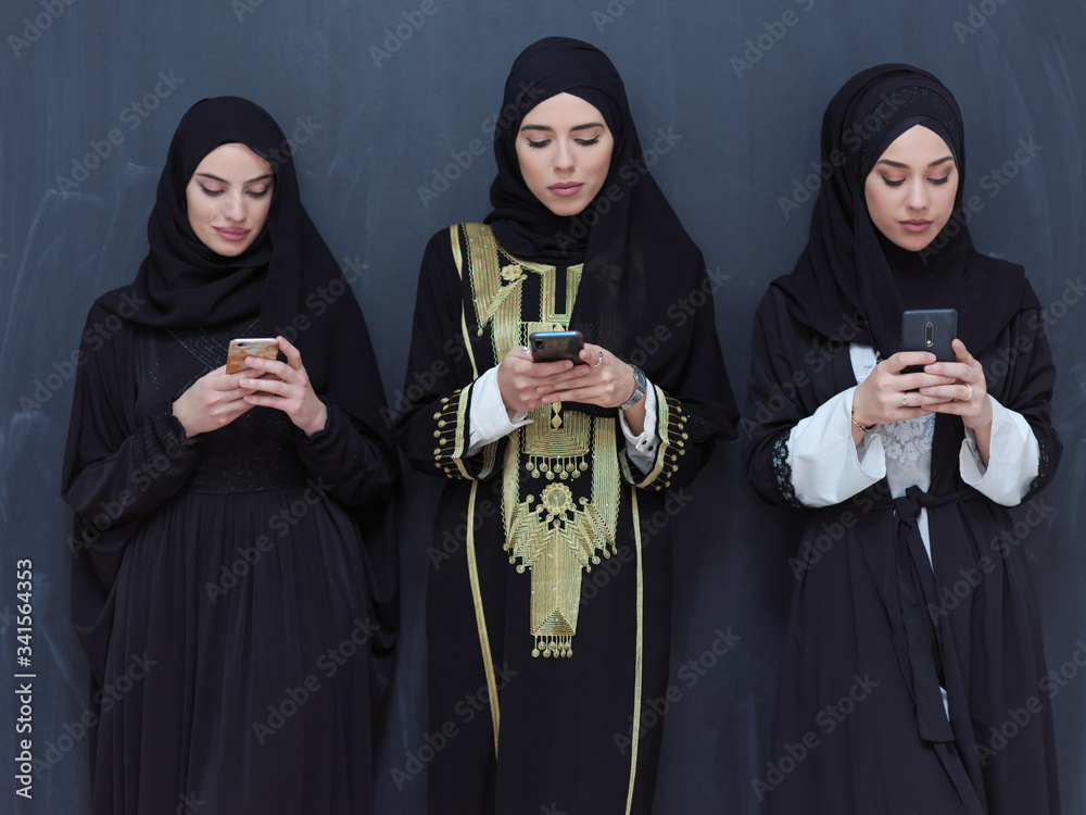 muslim women using mobile phone in front of black chalkboard muslim women using mobile phone in front of black chalkboard