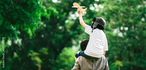 Panoramic background of father and son on his shoulder playing paper plane, spending time together at fresh green park in afternoon sunlight, the concept of family outdoor, daddy hero. Single Daddy.